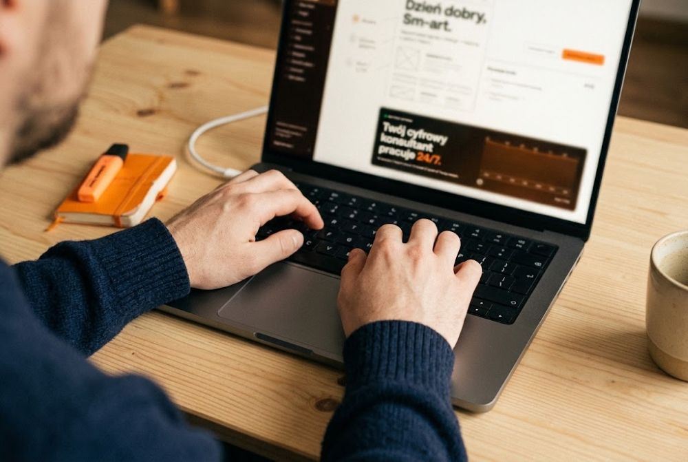 Laptop z otwartym projektem strony firmowej: menu z podstronami, nagłówek i blok z przyciskiem, obok notes i zakreślacz